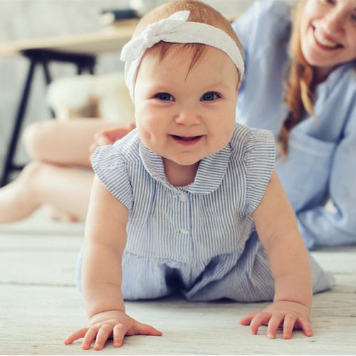 Smiling baby crawls playfully; adult beams with joy, highlighting fertility success at RMA Michigan.